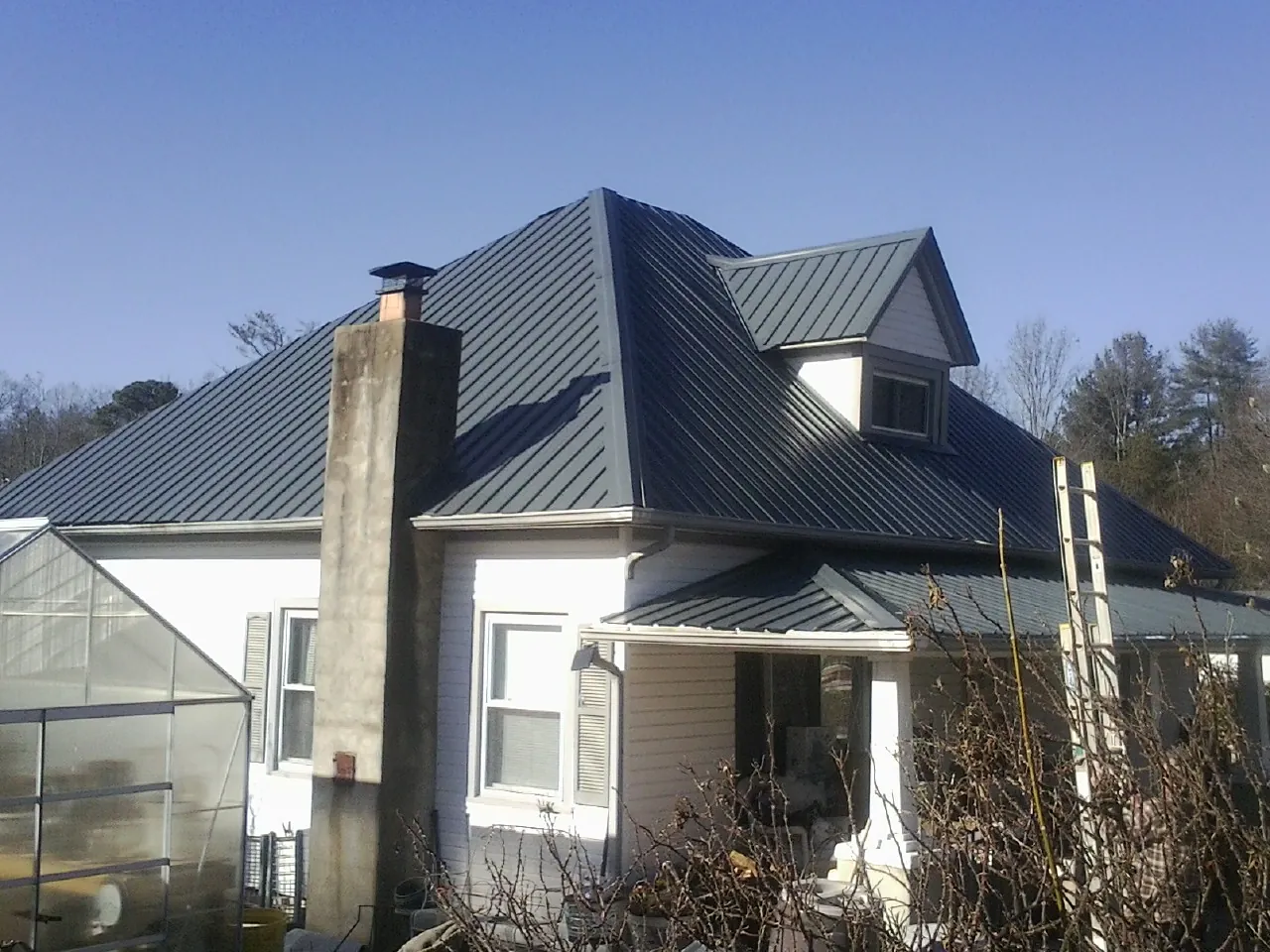 Dark blue standing seam metal roof on a white farmhouse with dormer — Slate & Tile Roof Repair by Roofing Brothers in Garden Plain