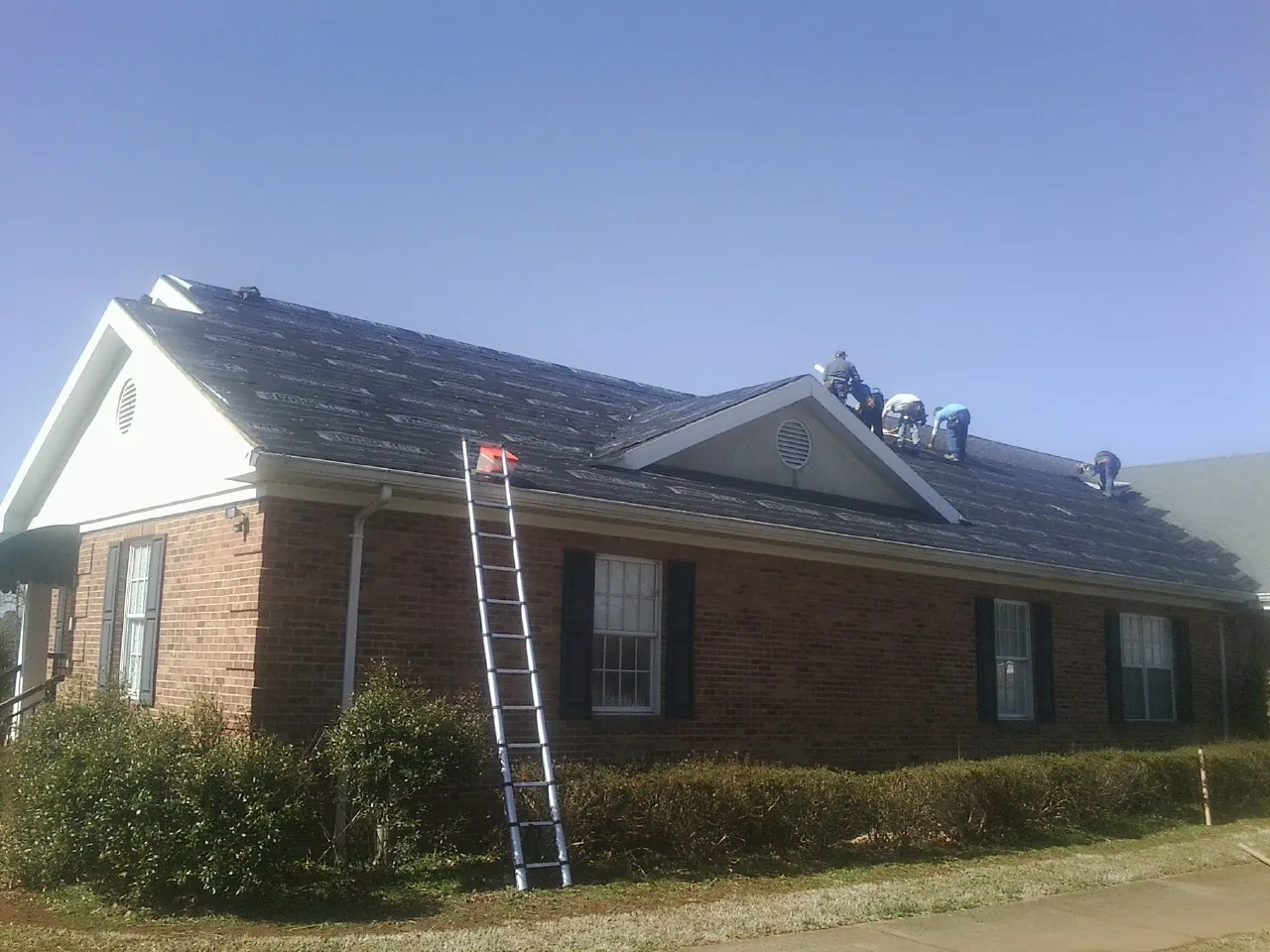 Crew tearing shingles off a brick ranch roof with a ladder set — Emergency Roof Repair work by our crew in Garden Plain