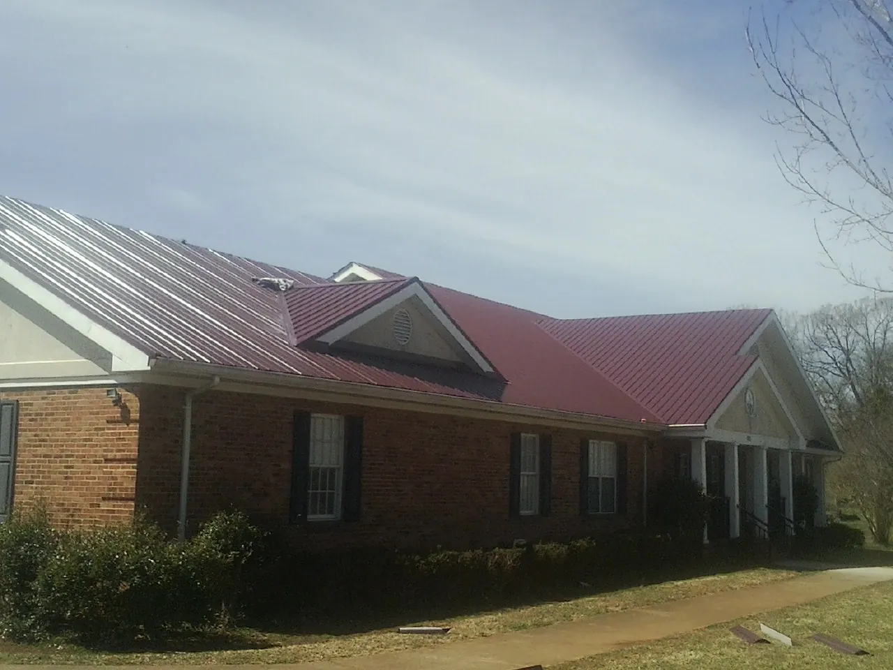 Red metal roof with gabled entries on a long brick building, from a Hail Damage Roof Repair job in Garden Plain