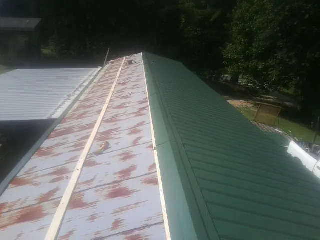 Old rusted panels beside newly installed green metal roofing — Wind Damage Roof Repair by Roofing Brothers in Garden Plain