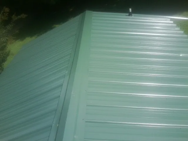 New green metal panels meeting at the ridge of a roof — Flat Roof Repair work by our crew in Garden Plain