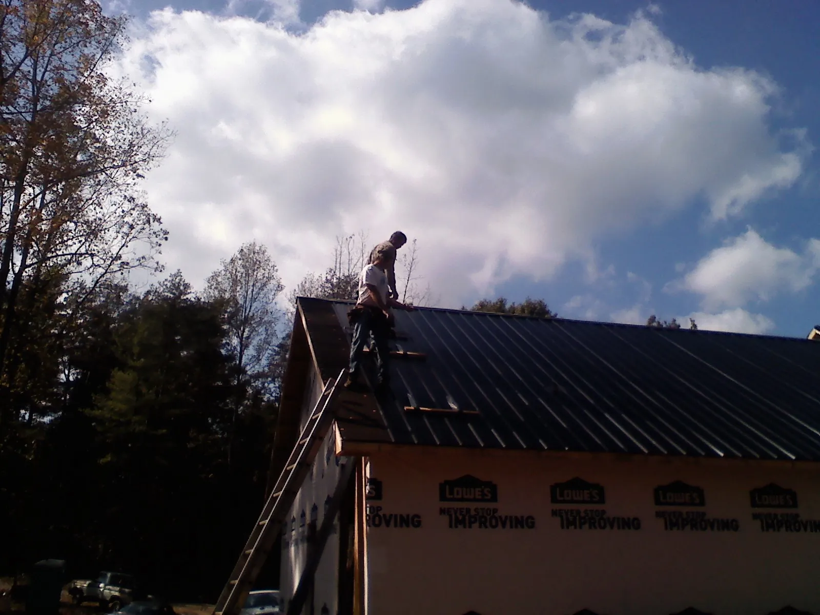Roofer fastening dark metal panels high against a cloudy sky, from a Roof Inspection job in Garden Plain