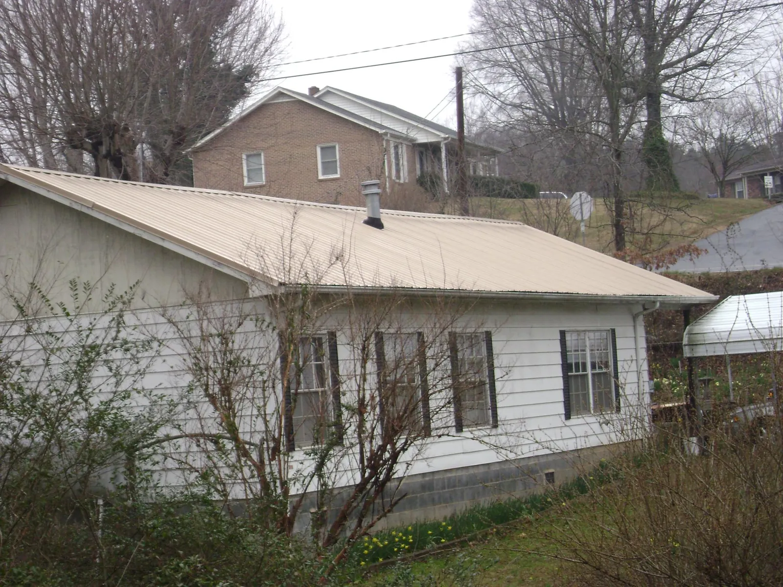 Tan metal roof on a white sided house set into a hillside — Commercial Roofing by Roofing Brothers in Garden Plain