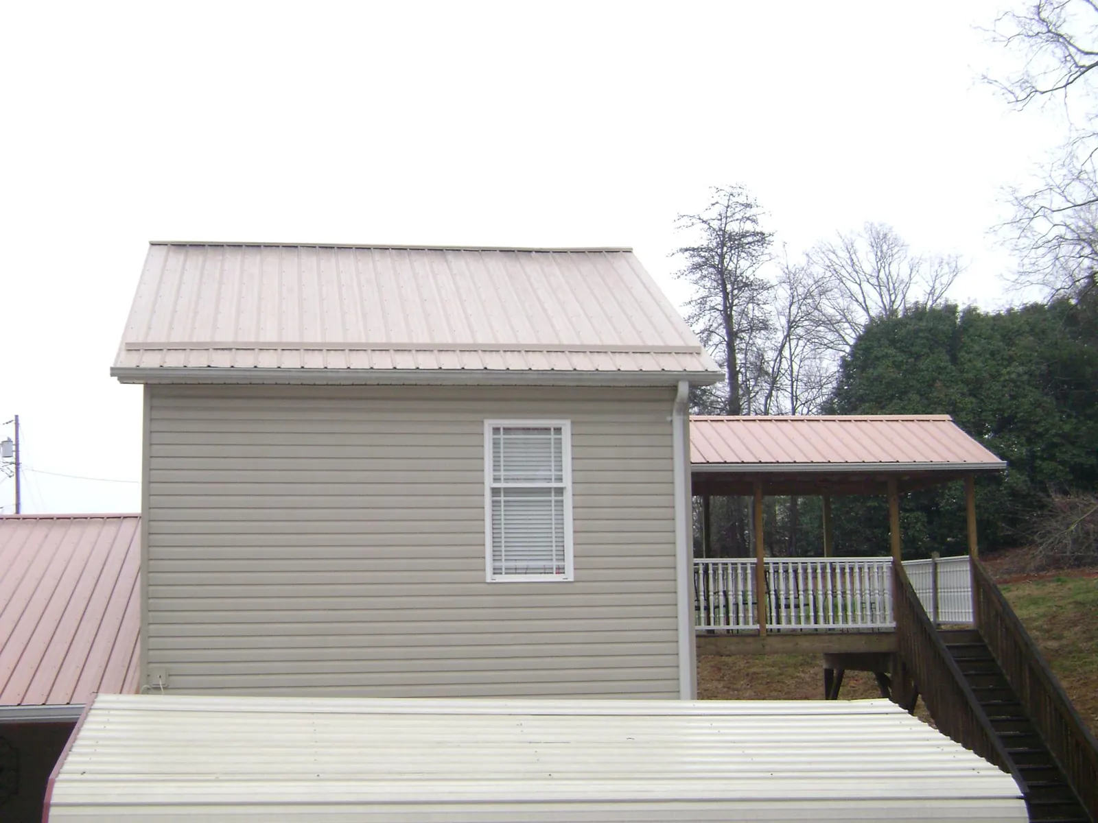Tan metal roofs on a two story addition and attached porch, from a Roof Replacement job in Garden Plain